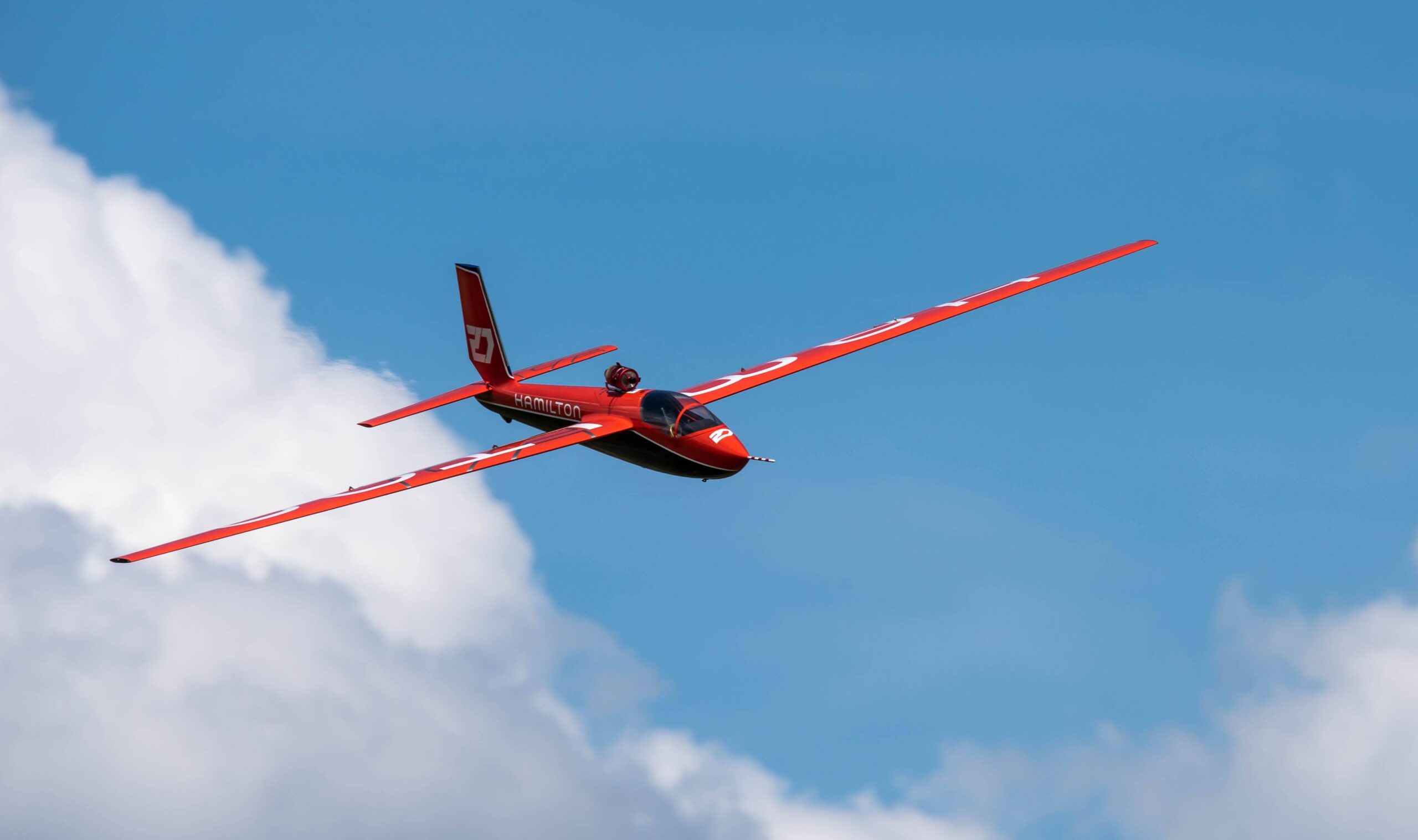Planeur radiocommandé rouge Hamilton en vol sur fond de ciel bleu